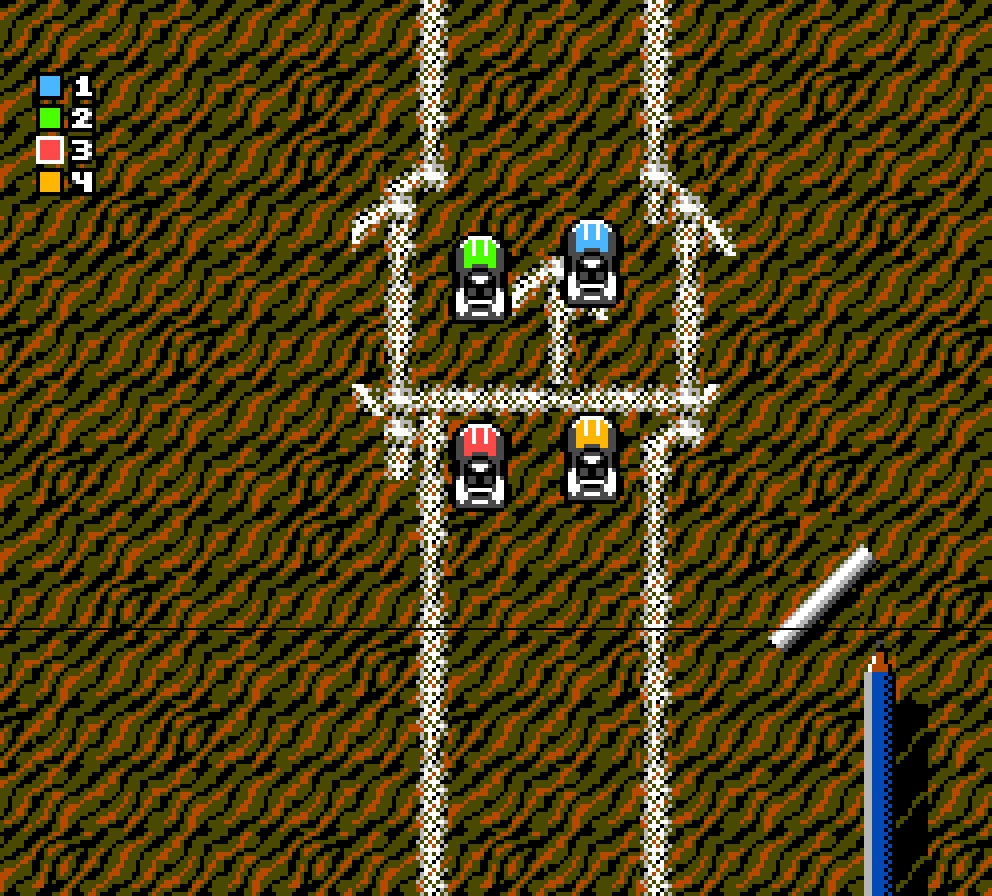 Four cars on the start grid in a sandpit, with a pencil lying by the track.